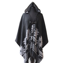 Load image into Gallery viewer, A black hooded shawl draped over a dress form. The shawl features a gray geometric design along the bottom half. It has a toggle button closure, gray lining, and fringe along the bottom hem.