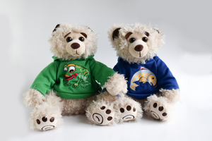 Two plush beige colored bears sit in front of a white background. The bear on the left has a green hoodie with a frog and the right bear has a blue hoodie with a salmon on it.