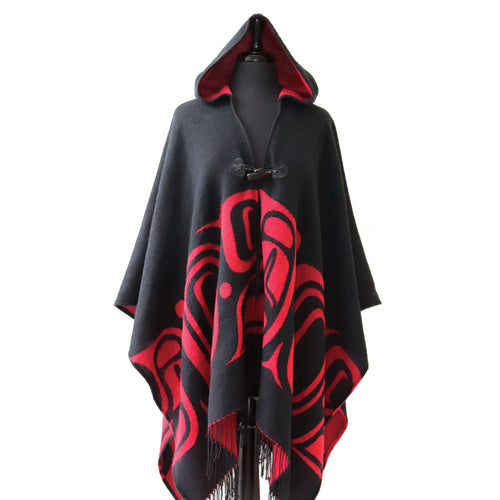 A black hooded Shawl draped over a dress form. The shawl has red formline designs alone the lower half and red lining. The shawl is closed by a toggle button. It has fringes along the bottom hem.